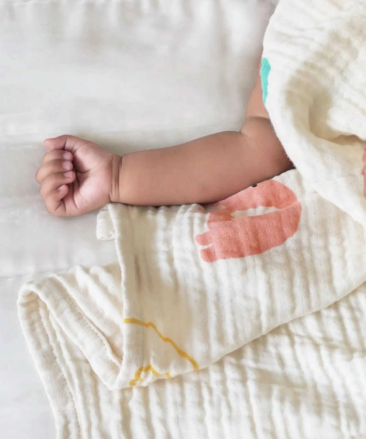 Baby arm wrapped in a soft baby swaddle with floral patterns on a white background