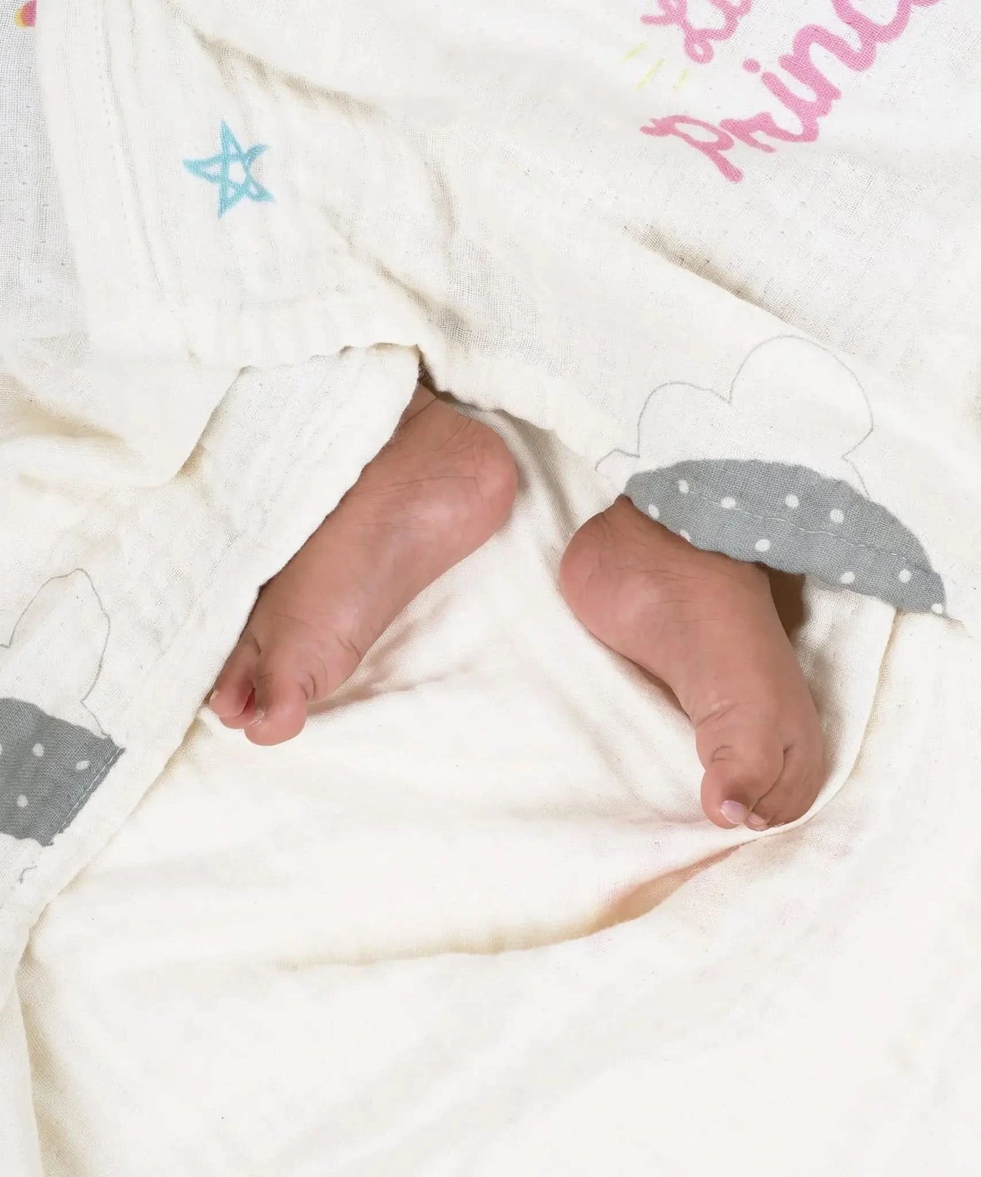 Baby feet peeking out from under a white blanket with gray cloud and star designs, and pink text.