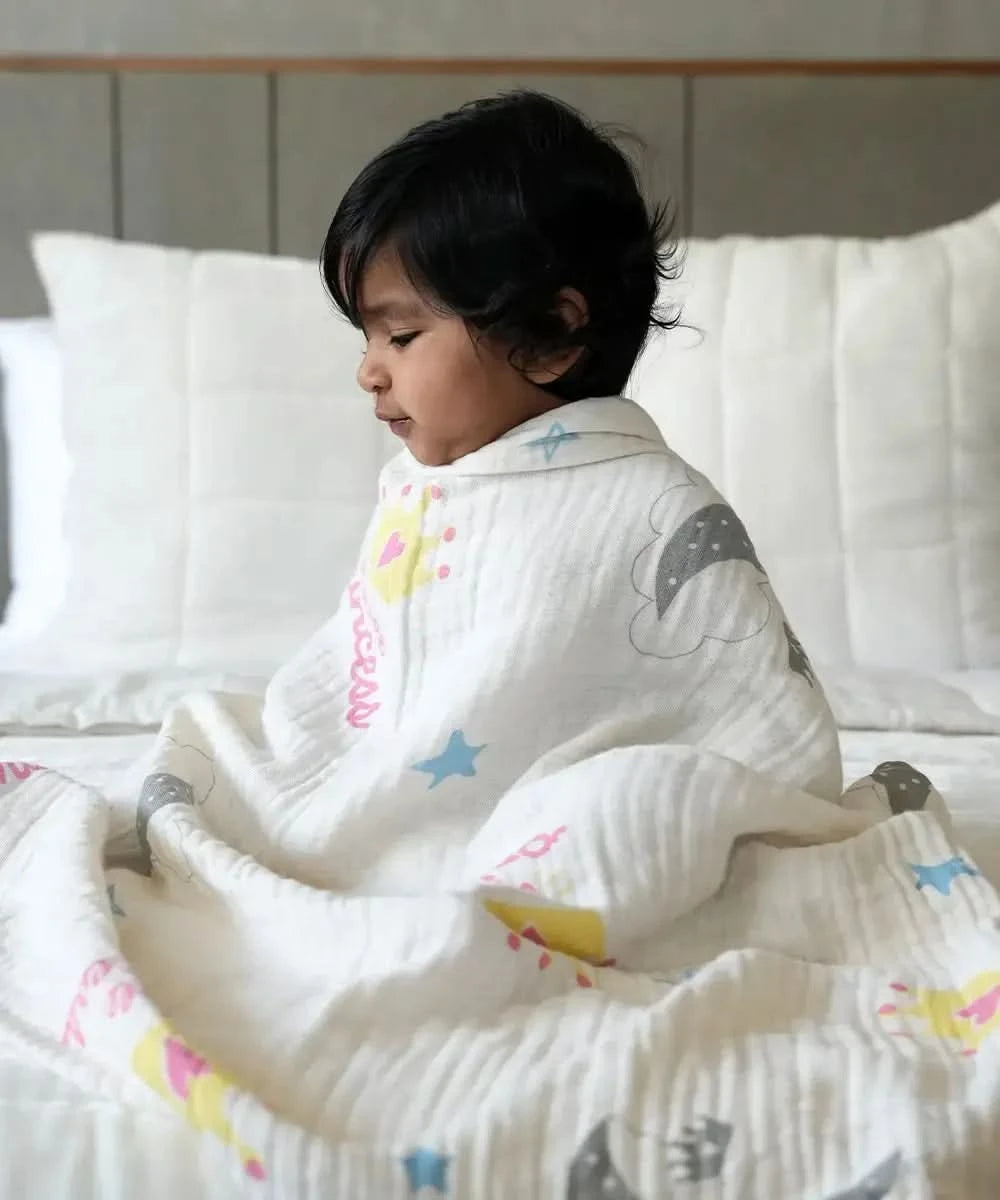 Child wrapped in a swaddle with colorful patterns sitting on a bed.