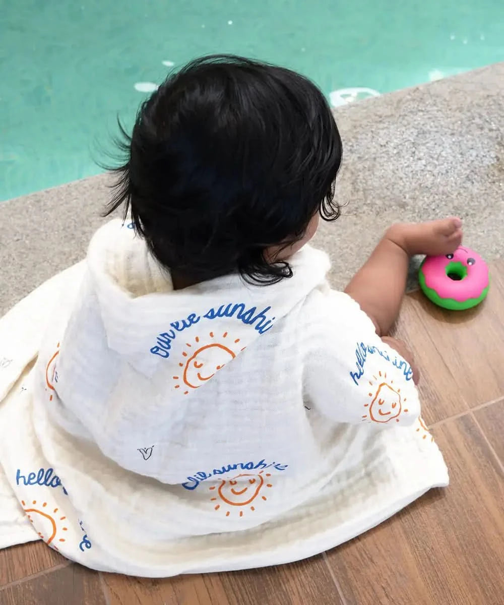 Child wrapped in a towel with 'hello sunshine' text, sitting by a pool.